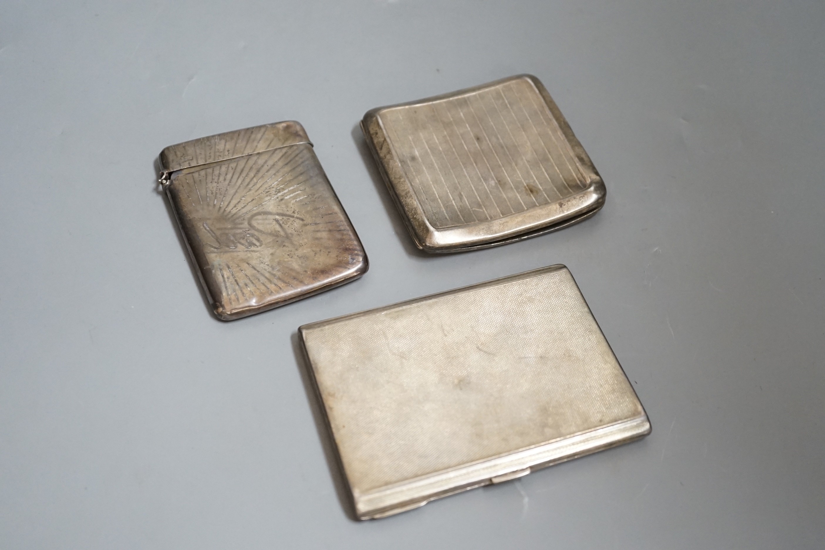 A George V engine turned silver cigarette case, 11.4cm, one other silver cigarette case and a silver card case with damaged lid.